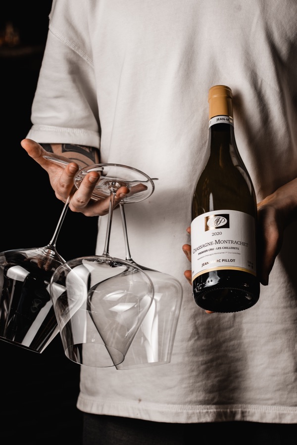 A sommelier carrying a bottle of Chassagne-Montrachet and empty glasses